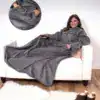 Poncho couverture polaire gris, capuche, poches, confortable sur canapé.