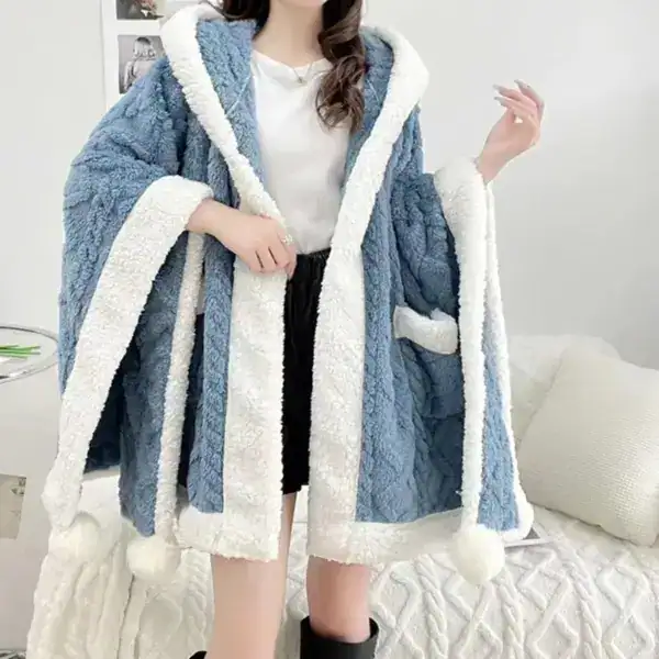 Poncho pilou pilou bleu avec capuche et pompons blancs.