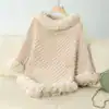 Poncho plaid beige à col et manches en fourrure synthétique, suspendu sur un cintre sur un canapé.