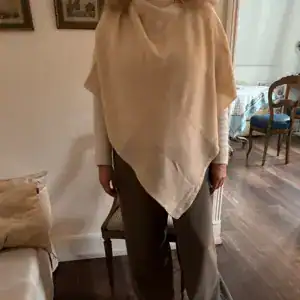 Poncho beige asymétrique porté sur un pantalon large