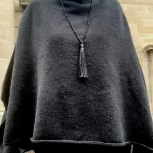 Poncho en maille noire porté avec un sautoir